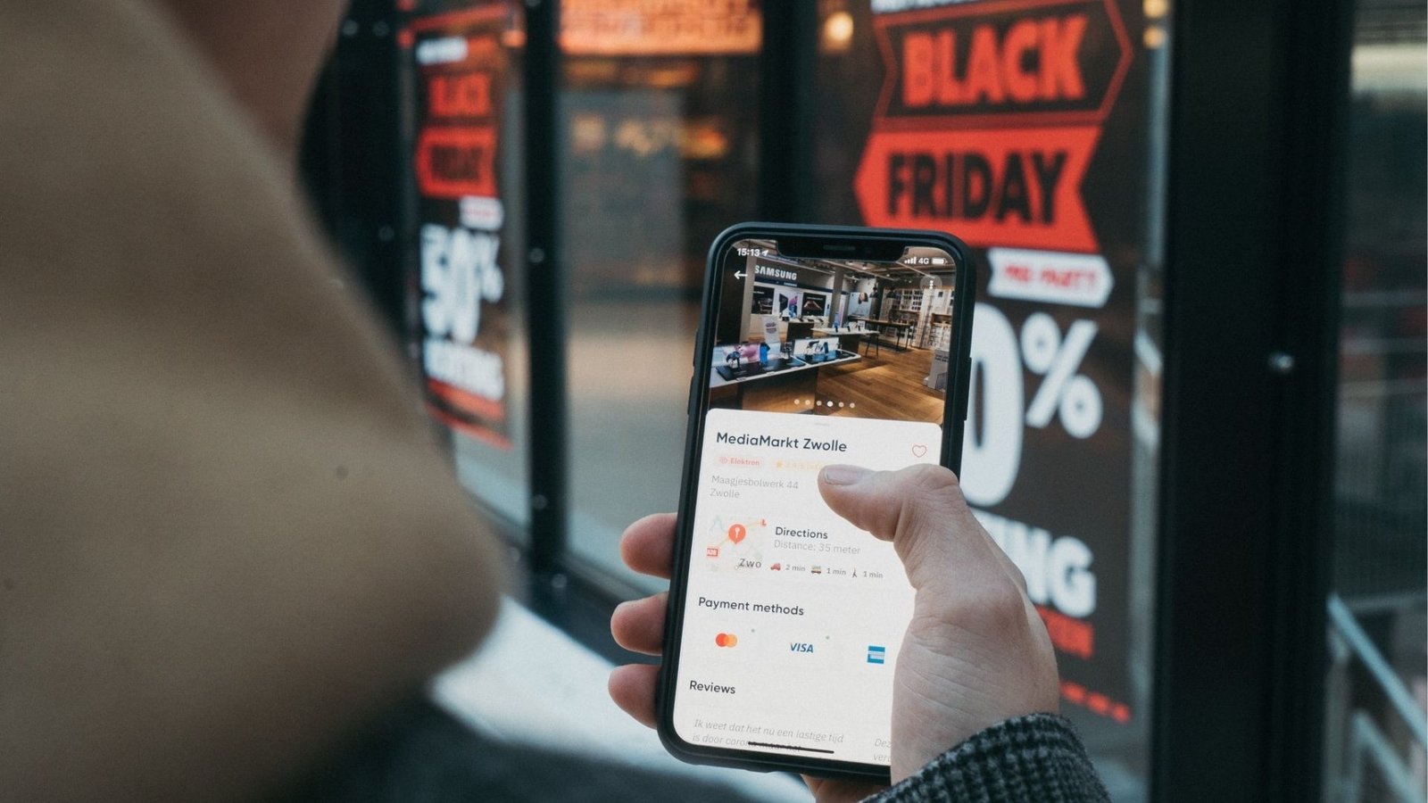 Imagem retirada de banco da internet, com um vitrine, um letreiro de led e uma pessoa mexendo no celular em busca de dicas da black friday